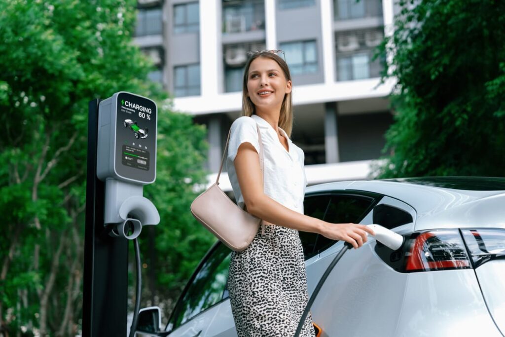 Sieviete lādē elektroauto parkingā